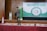 A young person stands on a stage holding a microphone. The backdrop features banners with text about character training, and a diagram with various values highlighted. The stage is covered with a patterned red carpet, and there's an Indonesian flag to one side.