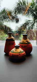 Brightly colored ceramic vases arranged on a windowsill with green plants around.