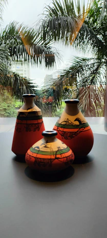 Brightly colored ceramic vases arranged on a windowsill with green plants around.