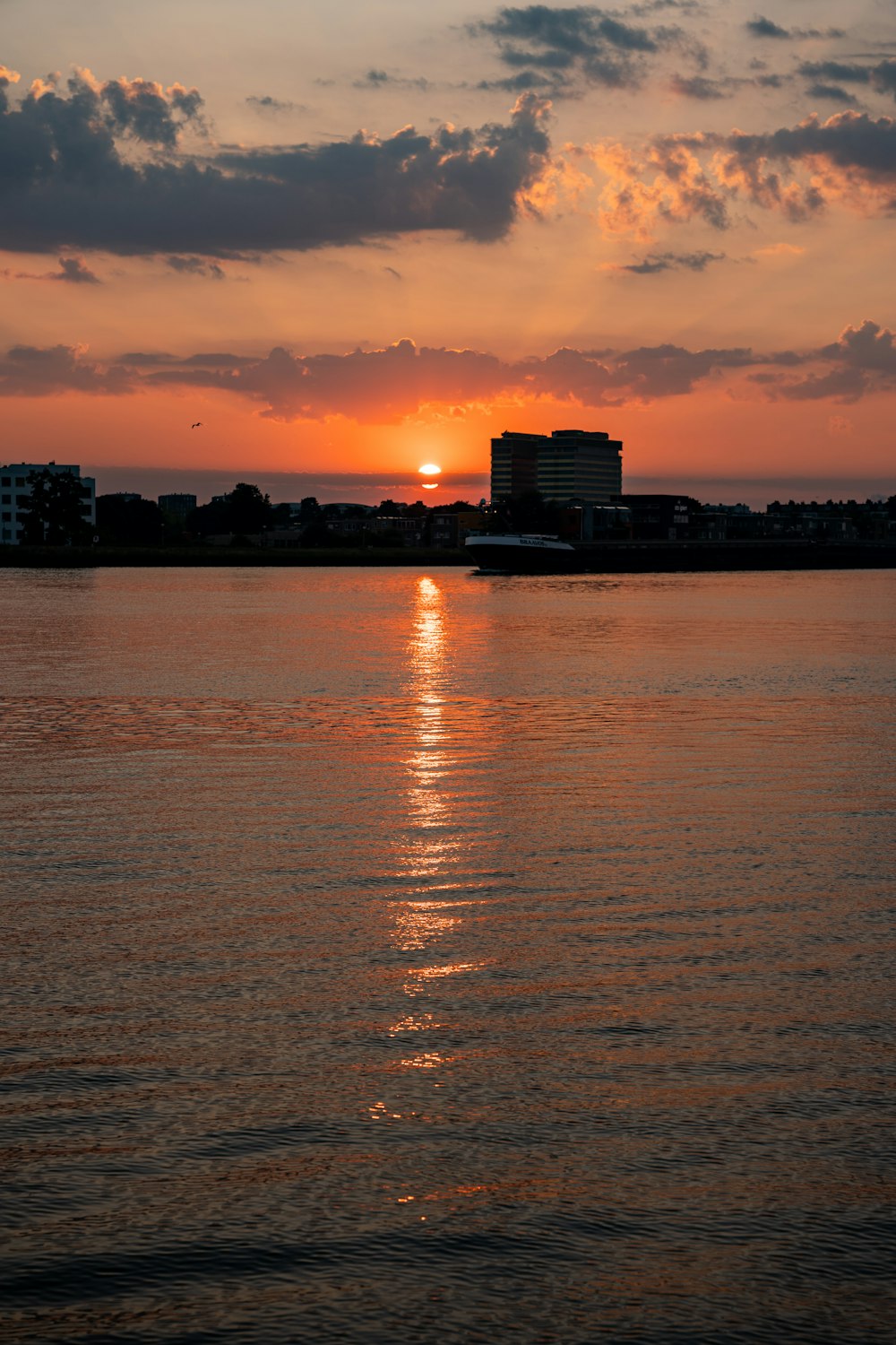 a body of water with buildings and a sunset in the background