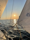 A serene sunset view from a sailboat gliding over calm blue waters.
