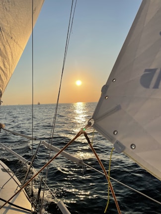 A serene sunset view from a sailboat gliding over calm blue waters.