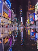 A vibrant urban nightlife scene with numerous brightly lit billboards and advertisements reflecting on a wet street surface. People are walking around, creating a lively atmosphere in a busy city square.