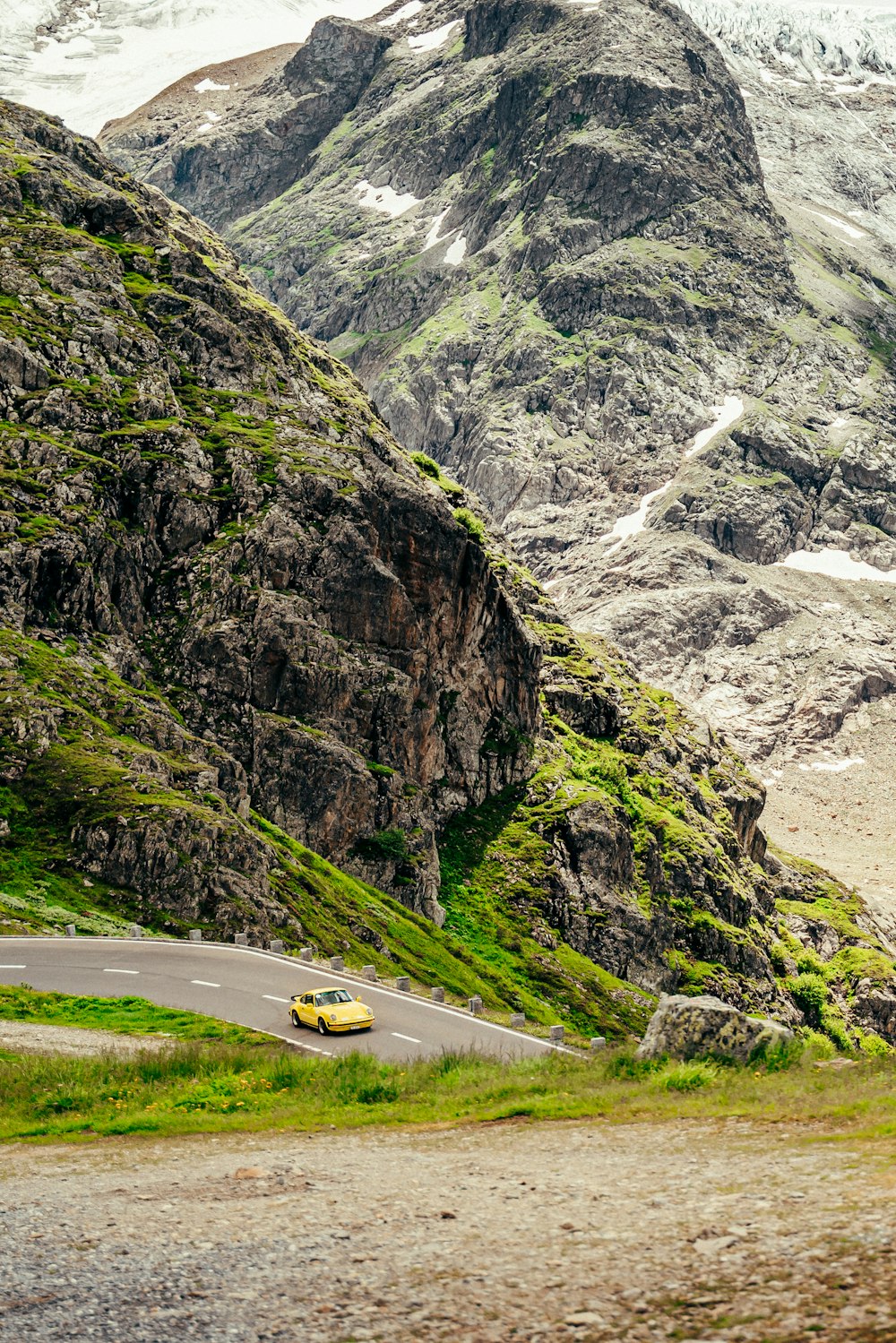 a yellow car driving on a road between mountains