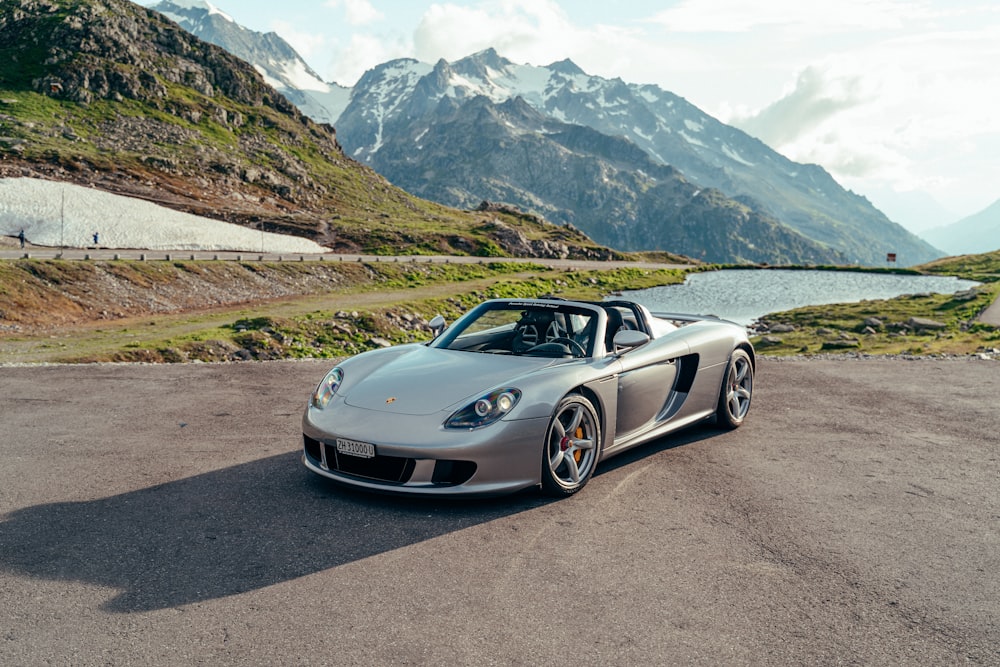 a silver sports car on a road with mountains in the background