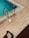 A swimming pool with turquoise water features stainless steel ladders on a wooden deck. The shadow of a person is visible on the deck, and the sunlight creates a warm and inviting atmosphere.