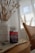 A bottle of Simply8 Gummy Vitamins, specifically B-Complex, sits on a wooden tabletop next to a white vase filled with decorative pampas grass. The scene includes a woven chair and a softly lit window with sheer curtains in the background, creating a calm and cozy atmosphere.