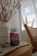 A bottle of Simply8 Gummy Vitamins, specifically B-Complex, sits on a wooden tabletop next to a white vase filled with decorative pampas grass. The scene includes a woven chair and a softly lit window with sheer curtains in the background, creating a calm and cozy atmosphere.