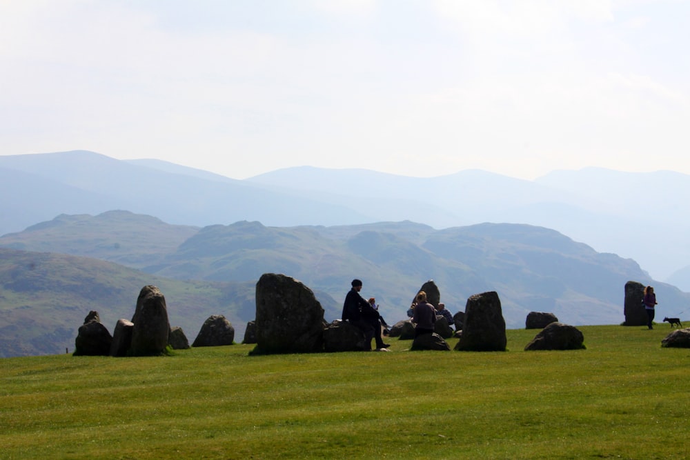 a group of people sitting on a rock formation in a grassy field