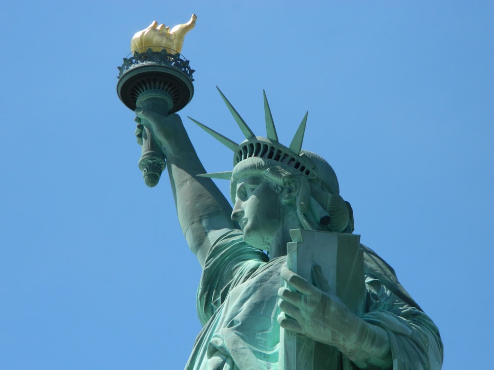 una statua di una persona che tiene una torcia con la Statua della Libertà sullo sfondo