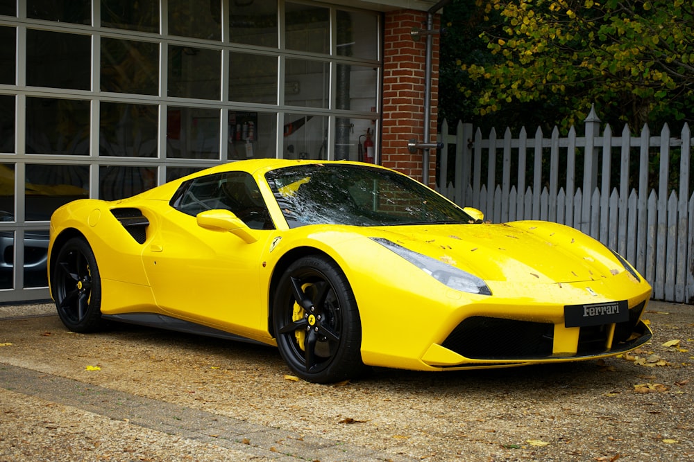 a yellow sports car parked in front of a white fence