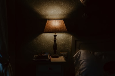 A bedside table lamp glowing softly next to a stack of books.