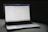 A MacBook Pro laptop displaying a webpage with a soft gray couch as a backdrop. The screen shows a website with text in the center, including a passage labeled 'Do Not Worry'. The laptop's backlit keyboard and touchpad are visible, and the bottom screen displays several application icons in the dock.
