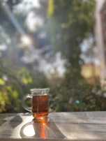 A peaceful morning scene with a steaming ceramic cup of tea beside a window, sunlight casting gentle shadows.