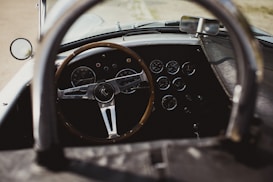 A vintage car interior featuring a wooden steering wheel and a dashboard with multiple round dials and gauges. The cockpit style design gives it a classic and elegant look.