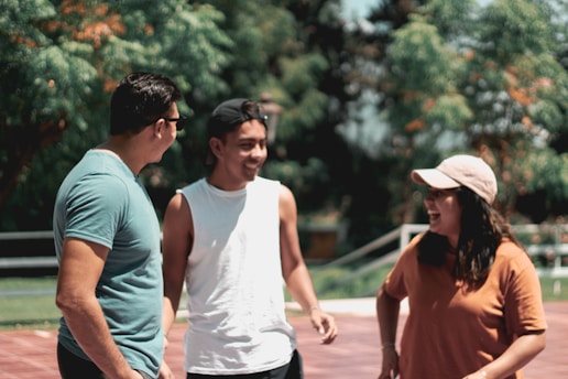 Three friends laughing together, each wearing a solé tri t-shirt in vibrant colors, standing against a sunlit urban backdrop.