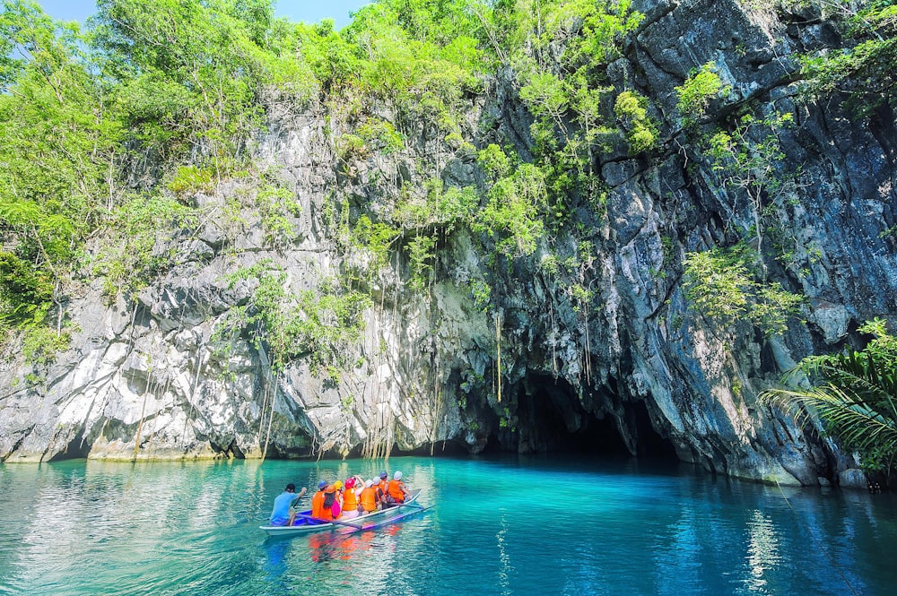a group of people in a boat in a body of water by a cliff with Puerto Princesa Subterranean River National Park in the background