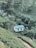 A small building with 'HYDRO POWER' written on its roof is surrounded by lush green tea plantations and trees. A narrow stream flows nearby, and terraced hills form a scenic backdrop with various shades of green.