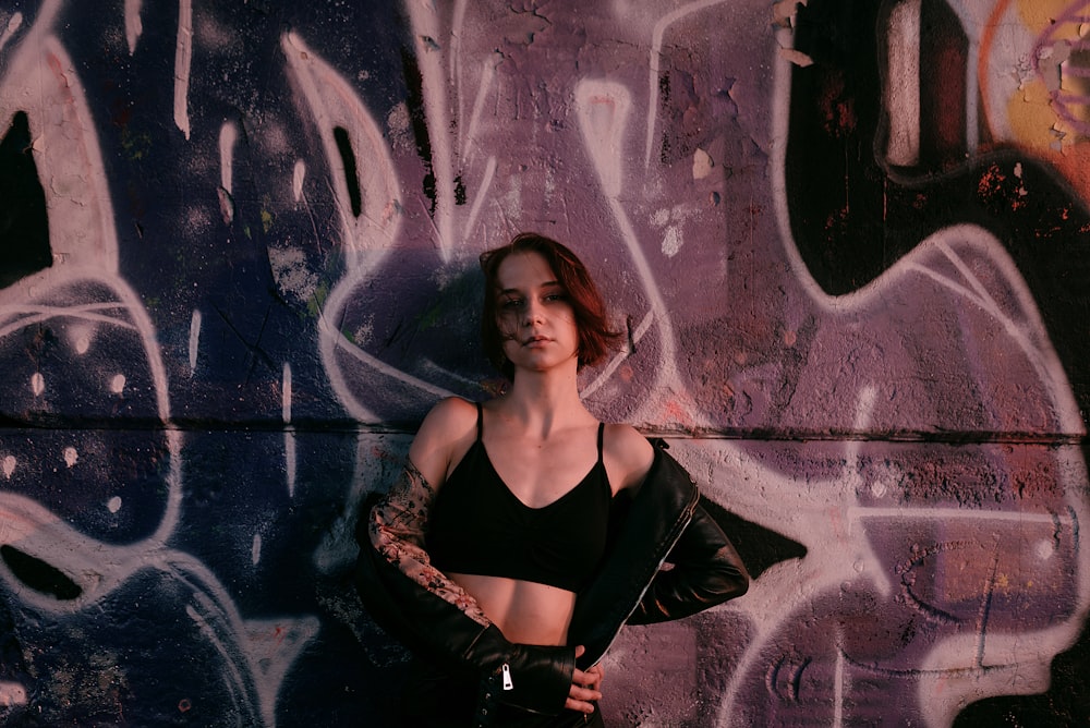 a woman posing in front of a wall covered in graffiti