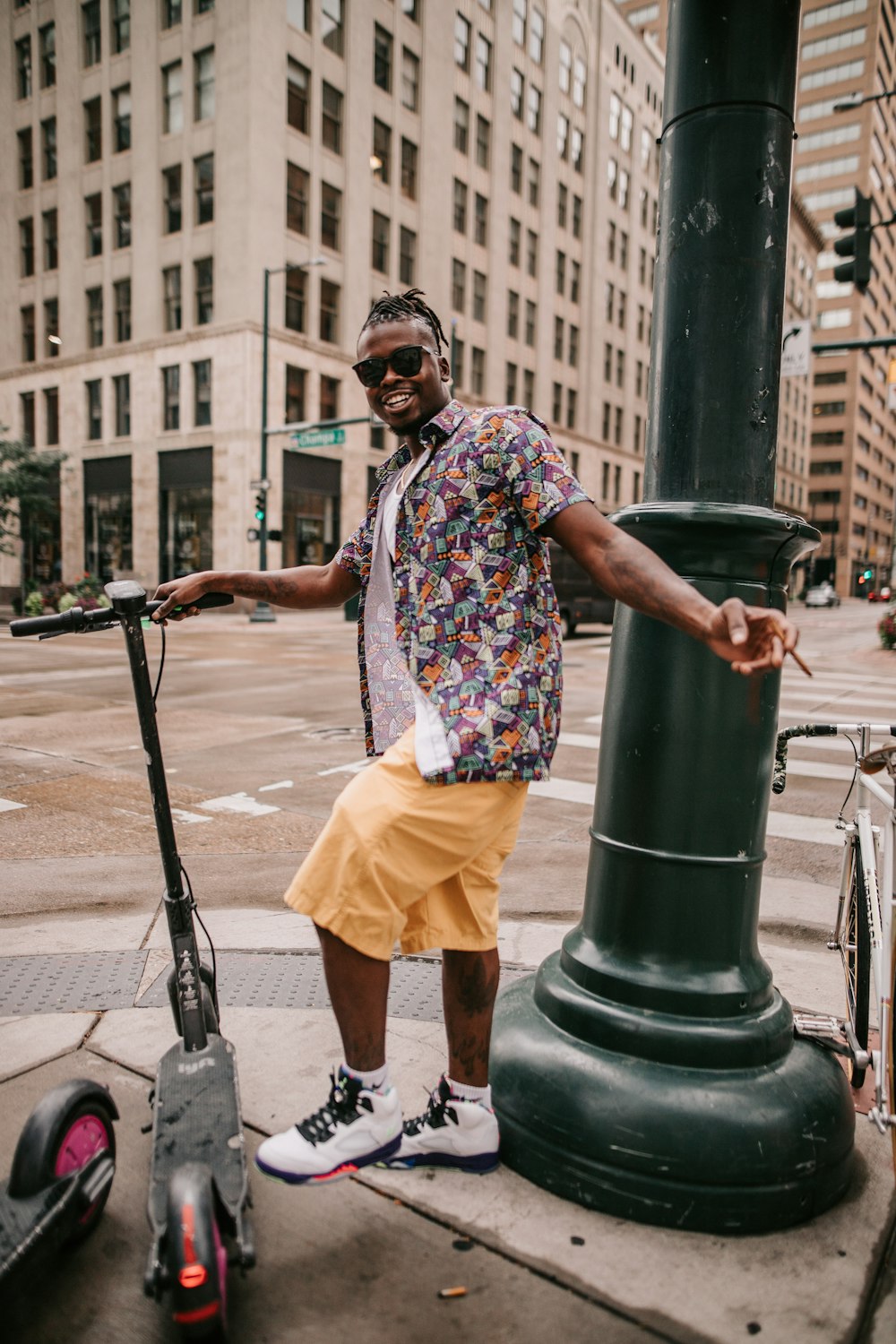 Un hombre con gafas de sol y una camisa colorida de pie junto a un poste verde