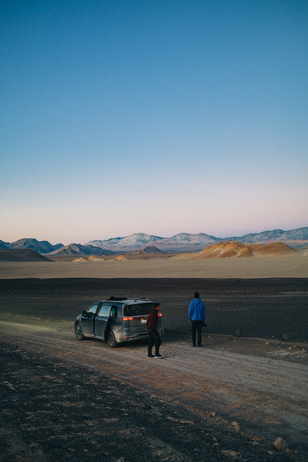 a couple of people standing next to a car in a desert
