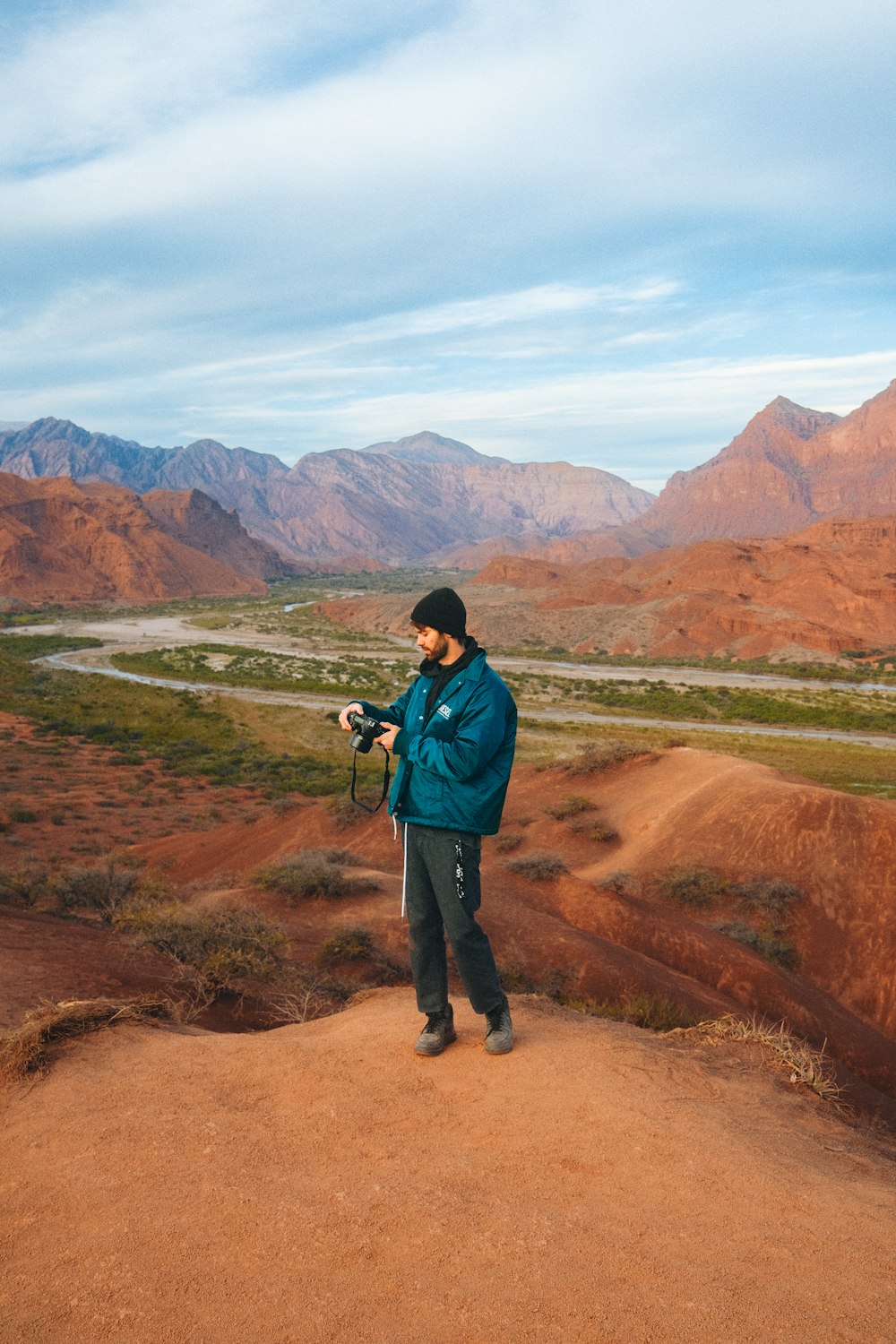 a man standing on a dirt road with mountains in the background