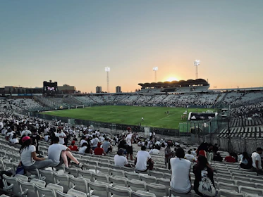 Wide shot of a packed stadium at dusk, with players warming up on the field.