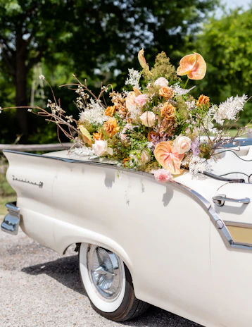 A cozy vintage car decorated with wedding flowers driving down a country road.