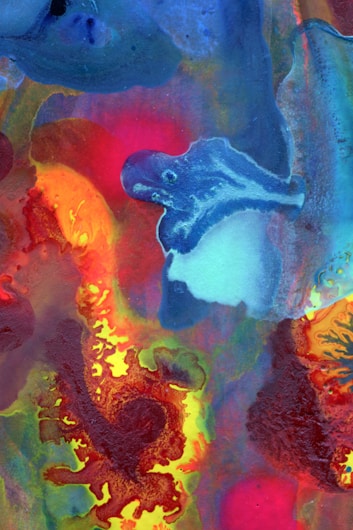 A vibrant and abstract painting featuring swirling shapes and colors, including shades of blue, red, orange, yellow, and green. The forms in the image appear fluid and organic, creating a dynamic and energetic composition.