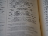 A close-up of an open book, focusing on a passage of religious text that advises singing to the LORD with grateful praise and making music to God on the harp. The text seems to be from a section of the Bible, displayed in crisp, readable font with slightly blurred pages in the background.