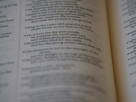 A close-up of an open book, focusing on a passage of religious text that advises singing to the LORD with grateful praise and making music to God on the harp. The text seems to be from a section of the Bible, displayed in crisp, readable font with slightly blurred pages in the background.