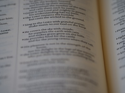 A close-up of an open book, focusing on a passage of religious text that advises singing to the LORD with grateful praise and making music to God on the harp. The text seems to be from a section of the Bible, displayed in crisp, readable font with slightly blurred pages in the background.