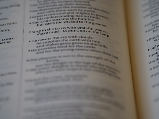 A close-up of an open book, focusing on a passage of religious text that advises singing to the LORD with grateful praise and making music to God on the harp. The text seems to be from a section of the Bible, displayed in crisp, readable font with slightly blurred pages in the background.