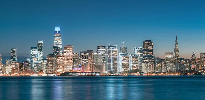 A vibrant city skyline at dusk with colorful lights reflecting on the water.