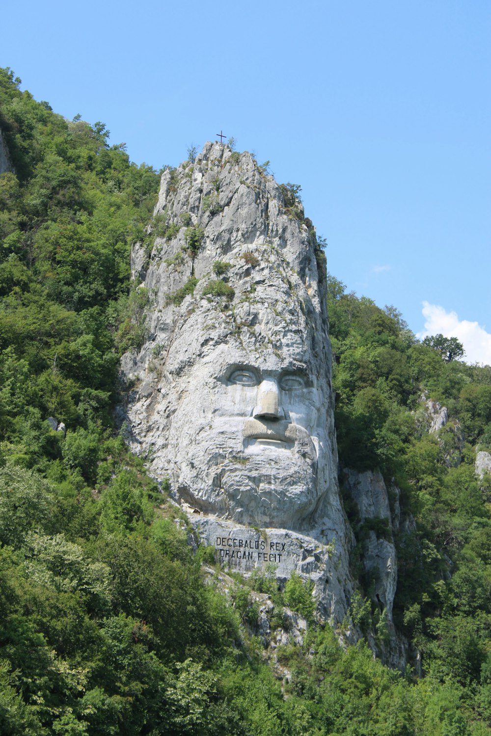 uma grande rocha com uma face esculpida nela com escultura de rocha de Decébalo no fundo