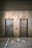 Two elevator doors made of metal are set within a wall, each with a small display panel above. The floor in front of the elevators has text and directional arrows marked on it, using a light-colored stencil style.