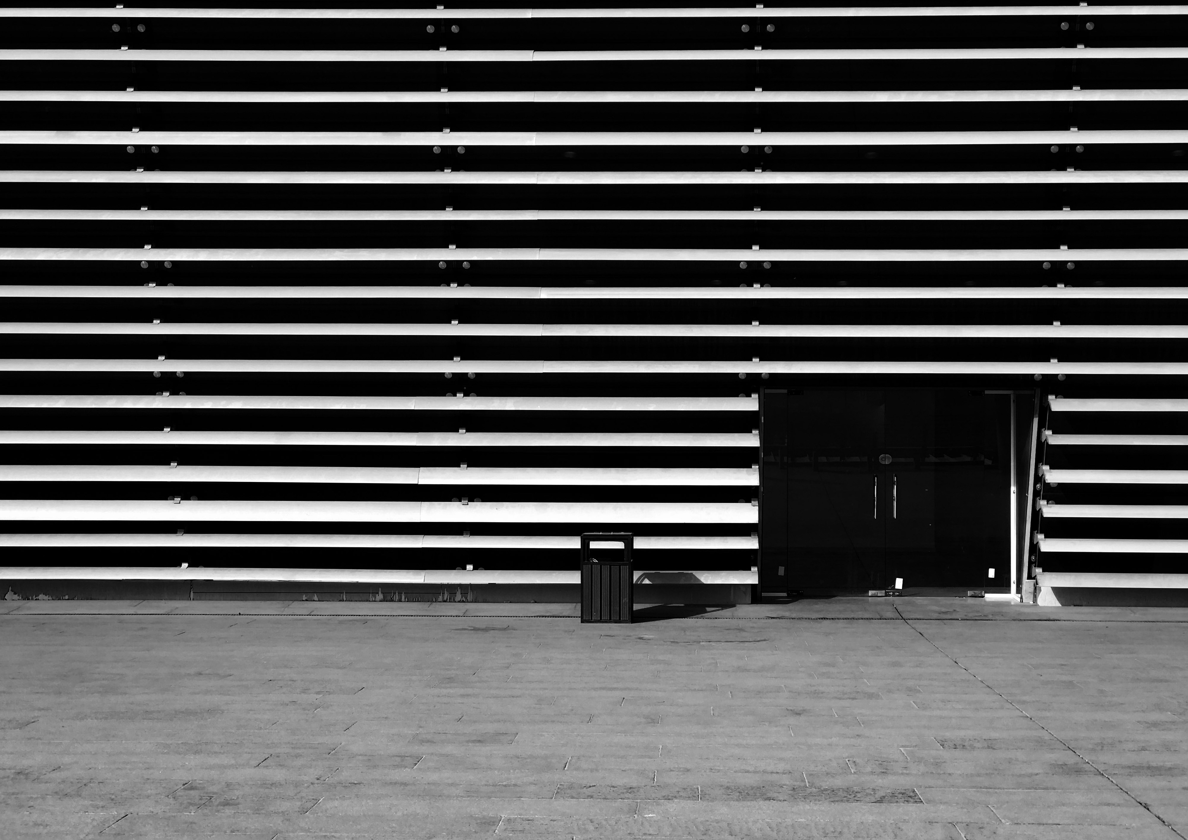 Black and white photograph of a building facade with strong horizontal lines and a single door. 