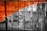 A large glass window with an abstract design featuring vibrant orange and black elements alongside white outlines. The window overlooks a street scene where people and a red vehicle can be seen blurred in the background.