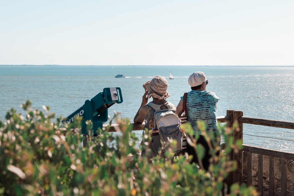 two people sitting on a bench looking at the ocean