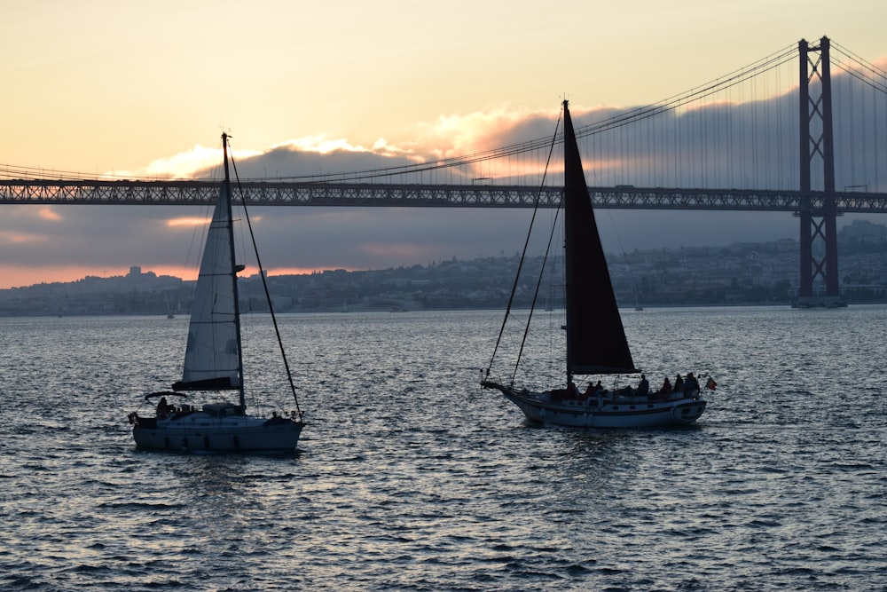 a couple of sailboats in front of a large bridge