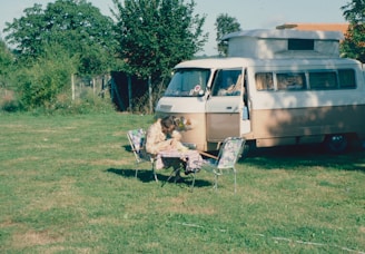 A person reading a guidebook about council regulations while sitting on the tailgate of a camper van.
