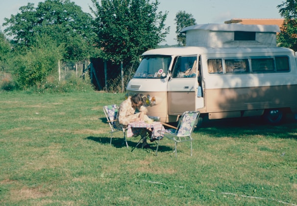 A person reading a guidebook about council regulations while sitting on the tailgate of a camper van.