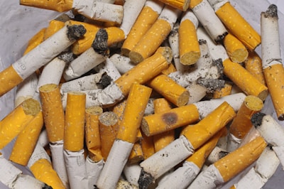 A pile of used cigarette butts with orange filters and white ash-covered paper, displaying signs of heavy use and ash debris.