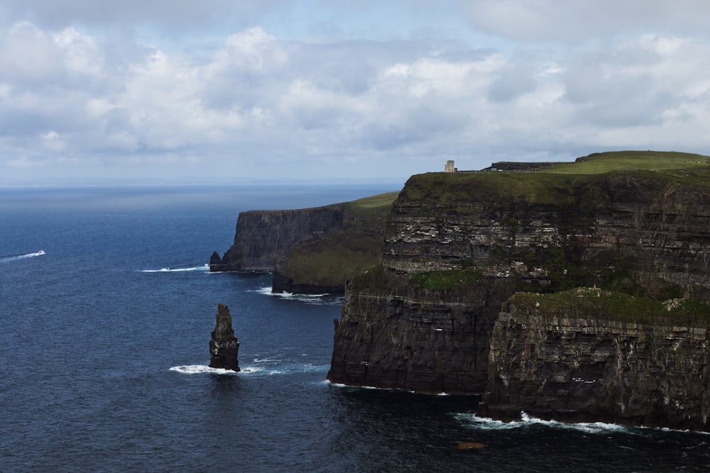 a cliff with a lighthouse on it with Cliffs of Moher in the background
