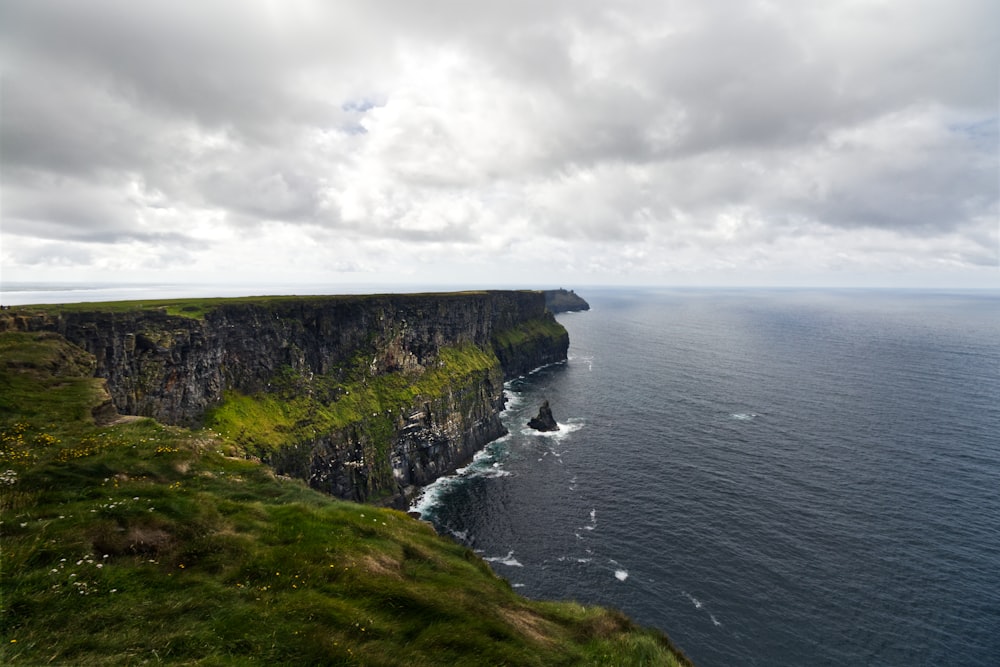 a cliff with a body of water below with Cliffs of Moher in the background
