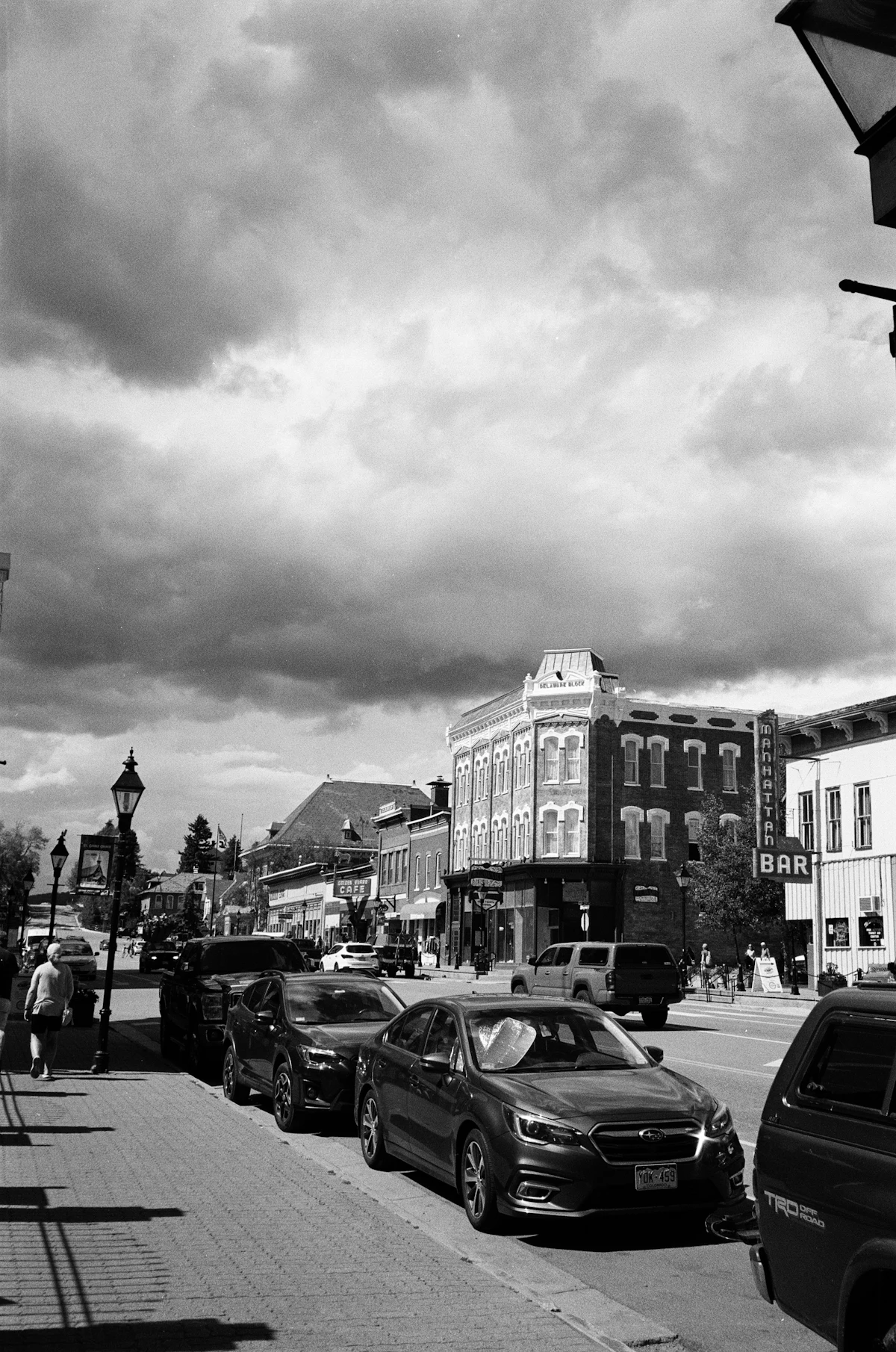 A black and white view of a Leadville street, with brick buildings and parked cars under heavy cloud