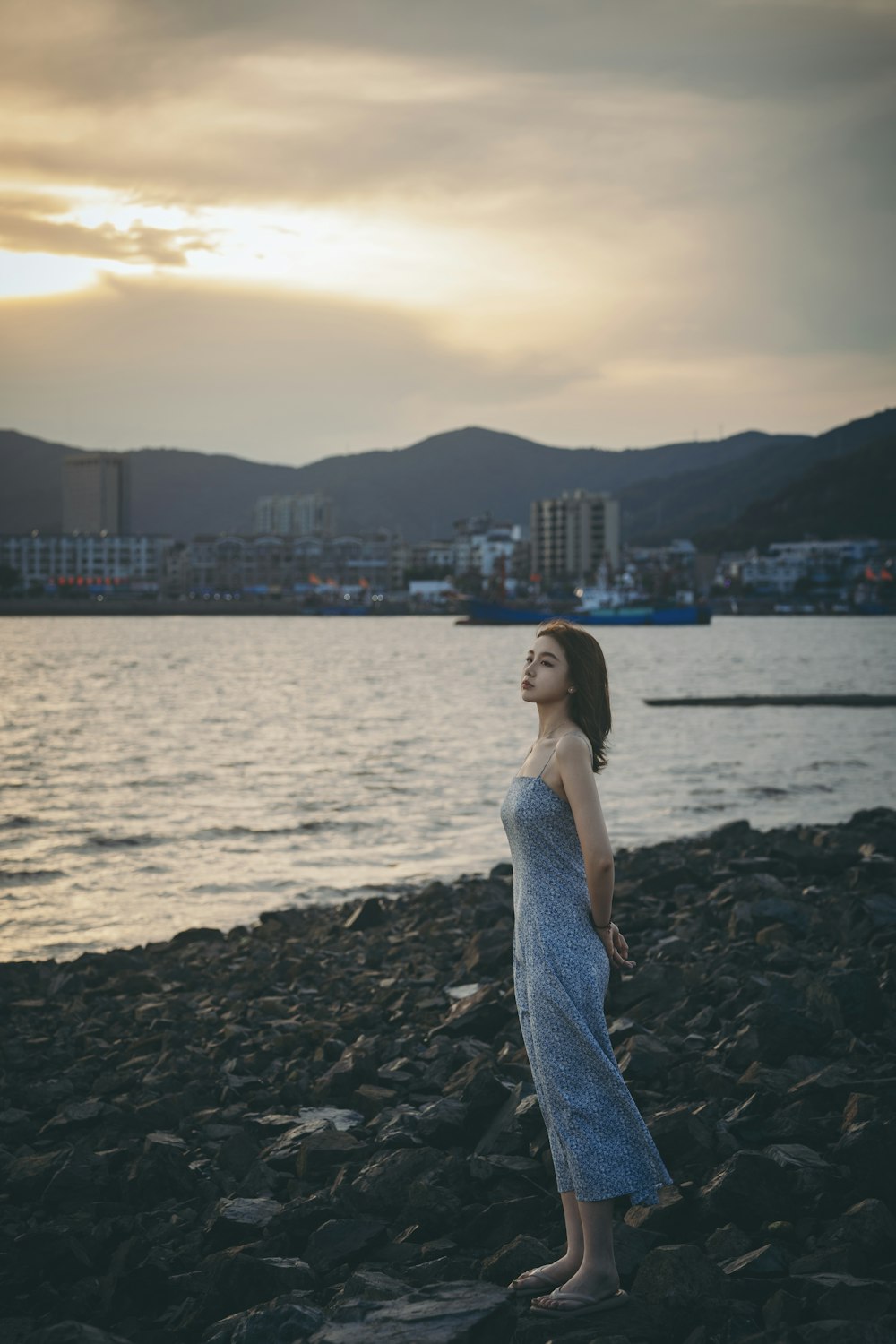 a man in a dress standing on a rocky beach with a city in the background