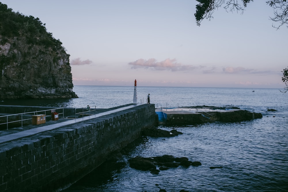 a stone wall with a walkway over water and a person standing on a rock wall