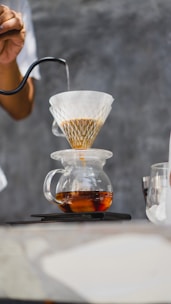 Barista pouring hot water over coffee grounds in a glass pour-over cone.