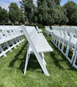 A spacious green lawn with white chairs arranged for an outdoor social gathering under a clear blue sky.